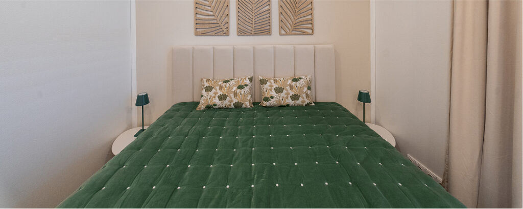 Schlafzimmer im 2B Mikrohaus mit grünem Bett, zwei Kissen und modernen Nachttischlampen.