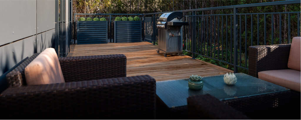 Sonnige Terrasse am 2B Mikrohaus mit Sitzgruppe, Holzboden und Grill.