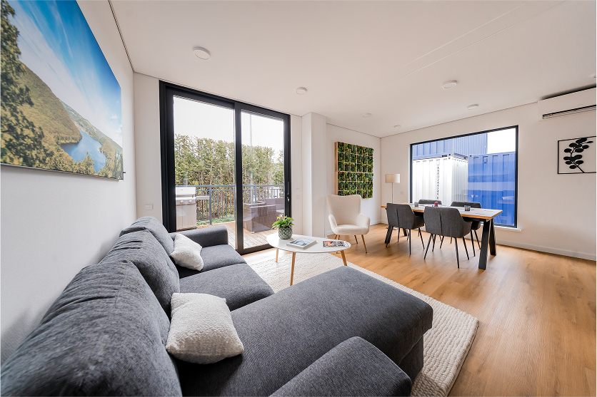 Helles Wohnzimmer im 2B Mikrohaus mit großer Couch, Essbereich und Zugang zur Terrasse.