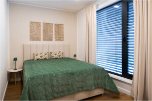 Schlafzimmer im 2B Mikrohaus mit großem Fenster, grünem Bett und moderner Wanddeko.