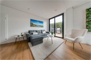 Wohnzimmer im 2B Mikrohaus mit grauem Sofa, Teppich, Sessel und Zugang zur Terrasse.